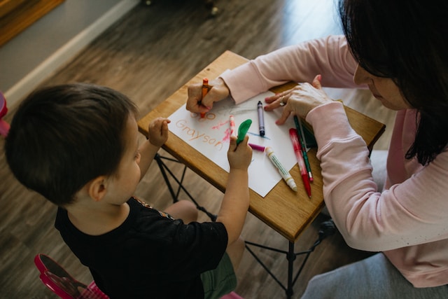 nursery teacher helping a kid with a drawing task on a table